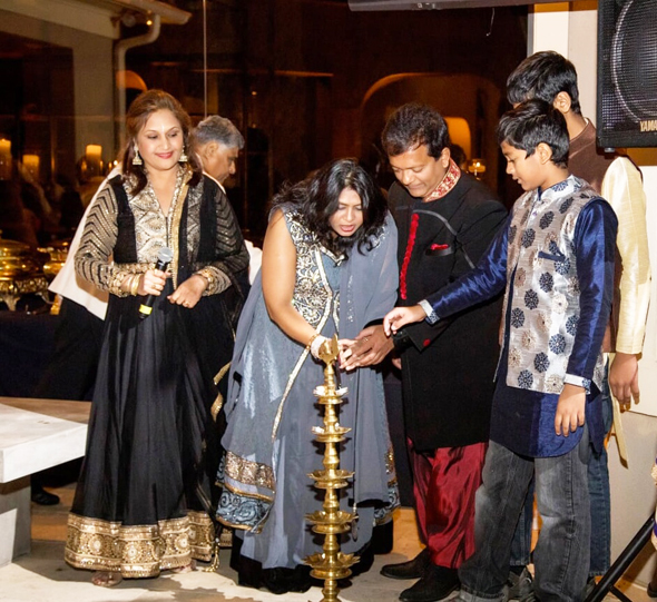 Leena and Ash Shah (center) and their two sons light the traditional Diwali diya to signify the festival of lights under the watchful eye of event co-chair Alpa Shah (left).